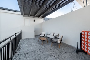 A covered patio area with a stone floor, two white sofas, a wooden coffee table, and a black and white patterned chair. - Two homes in one! Beautiful Courtyard with Pool! (Hurricane)