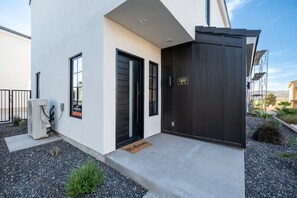 A modern building with a black door, a welcome mat, and a small air conditioning unit.
