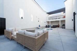 Une terrasse extérieure moderne, dotée de meubles en osier, d’une piscine et d’un espace abrité.