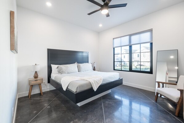 A modern bedroom with a bed, a ceiling fan, a window, and a chair.