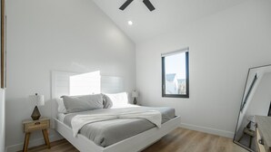 A modern bedroom with a white bed, a nightstand, a window, and a ceiling fan. - Two homes in one! Beautiful Courtyard with Pool! (Hurricane)