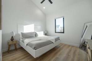 A modern bedroom with a white bed, a nightstand, a window, and a ceiling fan.
