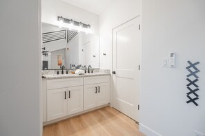 Un baño moderno con un espejo grande, tocador y zona de ducha.