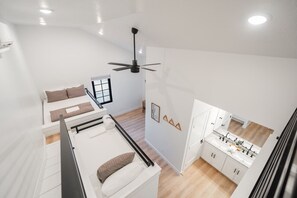 Un espacio habitable moderno y funcional con cama en altillo, kitchenette y ventilador de techo.