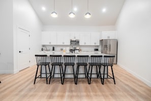 A modern kitchen with white cabinets, a central island with bar stools, a microwave, a refrigerator, and pendant lighting. - Two homes in one! Beautiful Courtyard with Pool! (Hurricane)