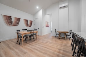 A spacious dining area with two wooden tables and black chairs, white walls, and a wooden floor. - Two homes in one! Beautiful Courtyard with Pool! (Hurricane)