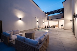 A modern outdoor patio with a pool, wicker furniture, and a balcony with a dining area.
