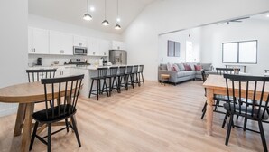 A modern kitchen with white cabinets, a central island with bar stools, and a dining area with a wooden table and chairs. - Two homes in one! Beautiful Courtyard with Pool! (Hurricane)