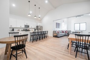Una cocina moderna con armarios blancos, una isla central con taburetes y una zona de comedor con una mesa y sillas de madera.
