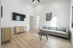 A modern living room with a flat-screen TV, a grey sofa, a wooden cabinet, and a coffee table.