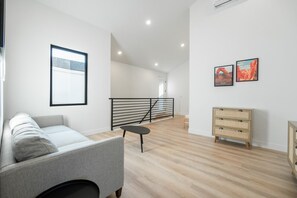 Una sala de estar moderna con un sofá, una mesita, una escalera y un cuadro colgado en la pared.