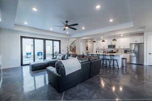 Un salon moderne avec un canapé en cuir foncé, un ventilateur de plafond et une grande porte-fenêtre coulissante donnant sur un balcon.