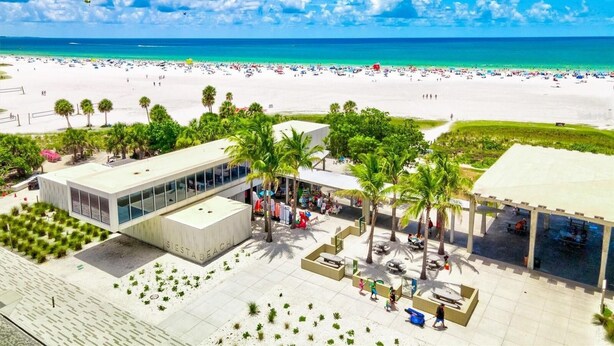Ein Hotel direkt am Strand mit modernem Design, das einen großzügigen Patio-Bereich mit Palmen, einen Pool und Blick auf den Strand und das Meer bietet.