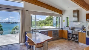 A modern kitchen with a large window overlooking a scenic view, a built-in oven, and a bar area with stools. - Absolute Beachfront Oneroa (Waiheke Island)