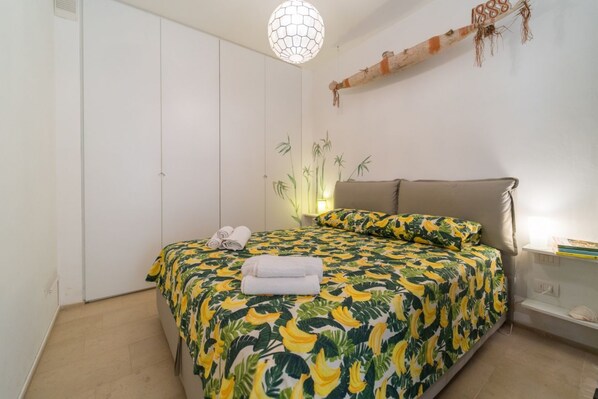 Un dormitorio con cama, armario, mesita de noche y estante en la pared.