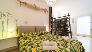 Une chambre à coucher avec un lit, des oreillers, une table de chevet, une lampe, une plante fixée au mur et une fenêtre.