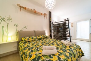 Une chambre à coucher avec un lit, des oreillers, une table de chevet, une lampe, une plante fixée au mur et une fenêtre.