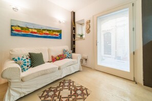 Una sala de estar con un sofá blanco, almohadones coloridos, un tapete estampado con estrellas, un cuadro de barcos y una puerta corrediza de vidrio.