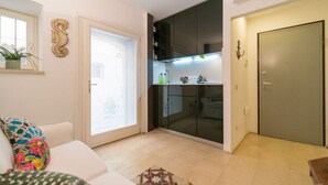 Un espace de vie compact comprenant un canapé, un tapis à motifs, un coin cuisine avec des placards et une porte.