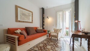 Una sala de estar con un sofá, un tapete estampado, una silla, una mesa y un cuadro en la pared.