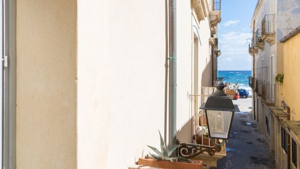 Una calle estrecha flanqueada por edificios, un farol y vista al mar en la distancia.