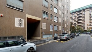 En byggnad med flera våningar, ett parkeringsområde, en överbyggd entré och en rad uppradade parkerade bilar.