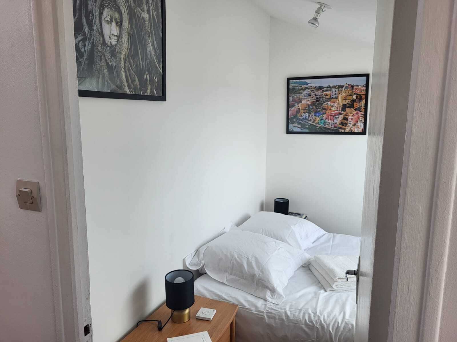 Una camera da letto con un letto, un comodino con una lampada e due quadri appesi al muro.