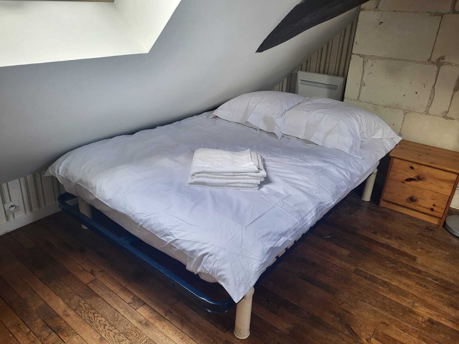 Ein kleines Zimmer mit einem Einzelbett, geneigter Decke, Holzboden und einem schlichten Nachttisch.