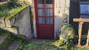 A rustic stone building with a red door, a small window, and a bell.