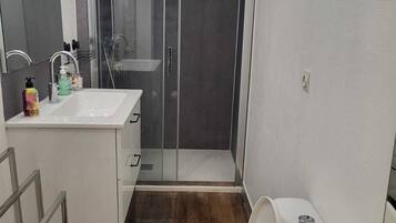 Un baño moderno con cabina de ducha de vidrio, un lavamanos blanco y un inodoro.
