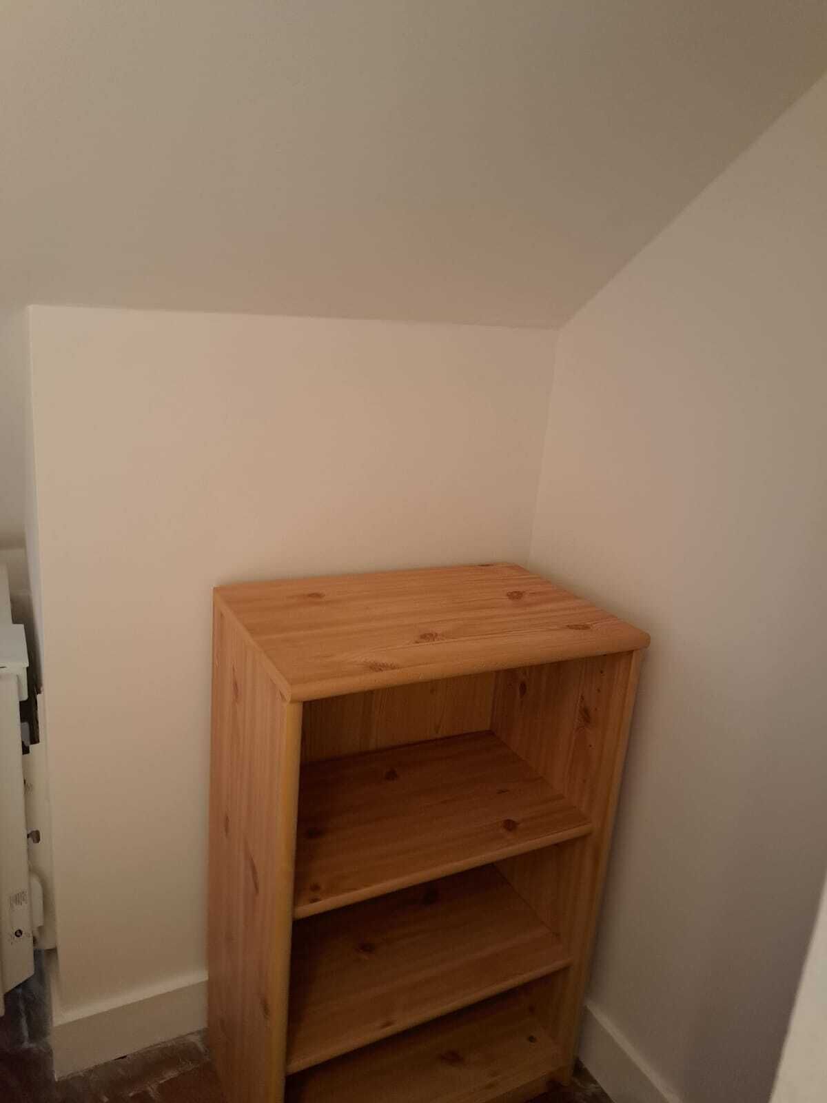 A corner room with a wooden shelf unit against the wall.
