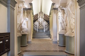 Un amplio pasillo con estatuas clásicas, una escalera central y suelo de mármol.