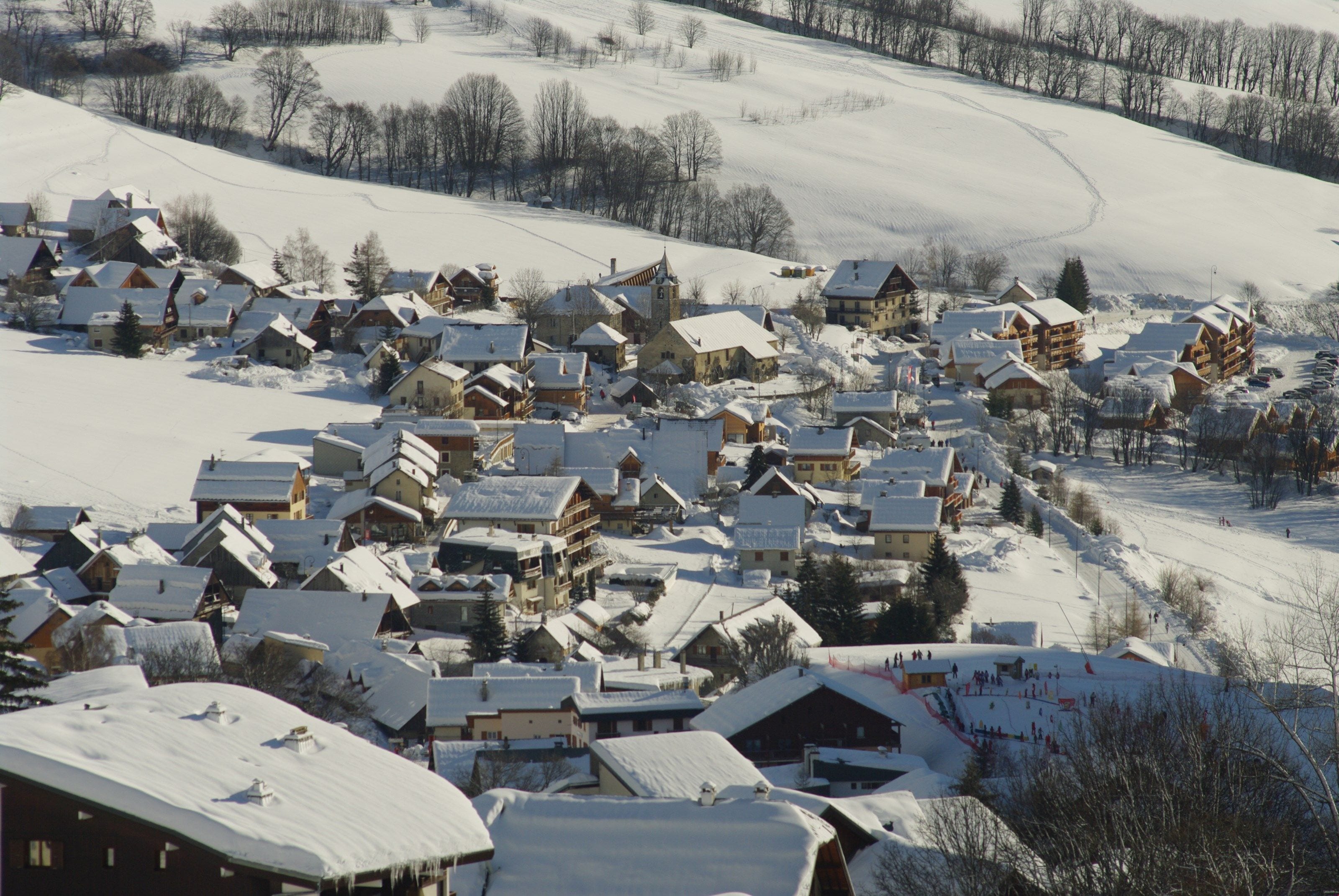 Un village enneigé, avec ses maisons traditionnelles en bois et une piste de ski.