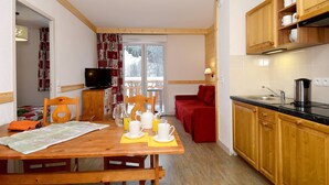 A cozy room with a wooden table set for breakfast, a television, and a red sofa. - Sleeps 6! Mountain Escape + Pool & Wi-Fi Access! (Saint Sorlin d'Arves)