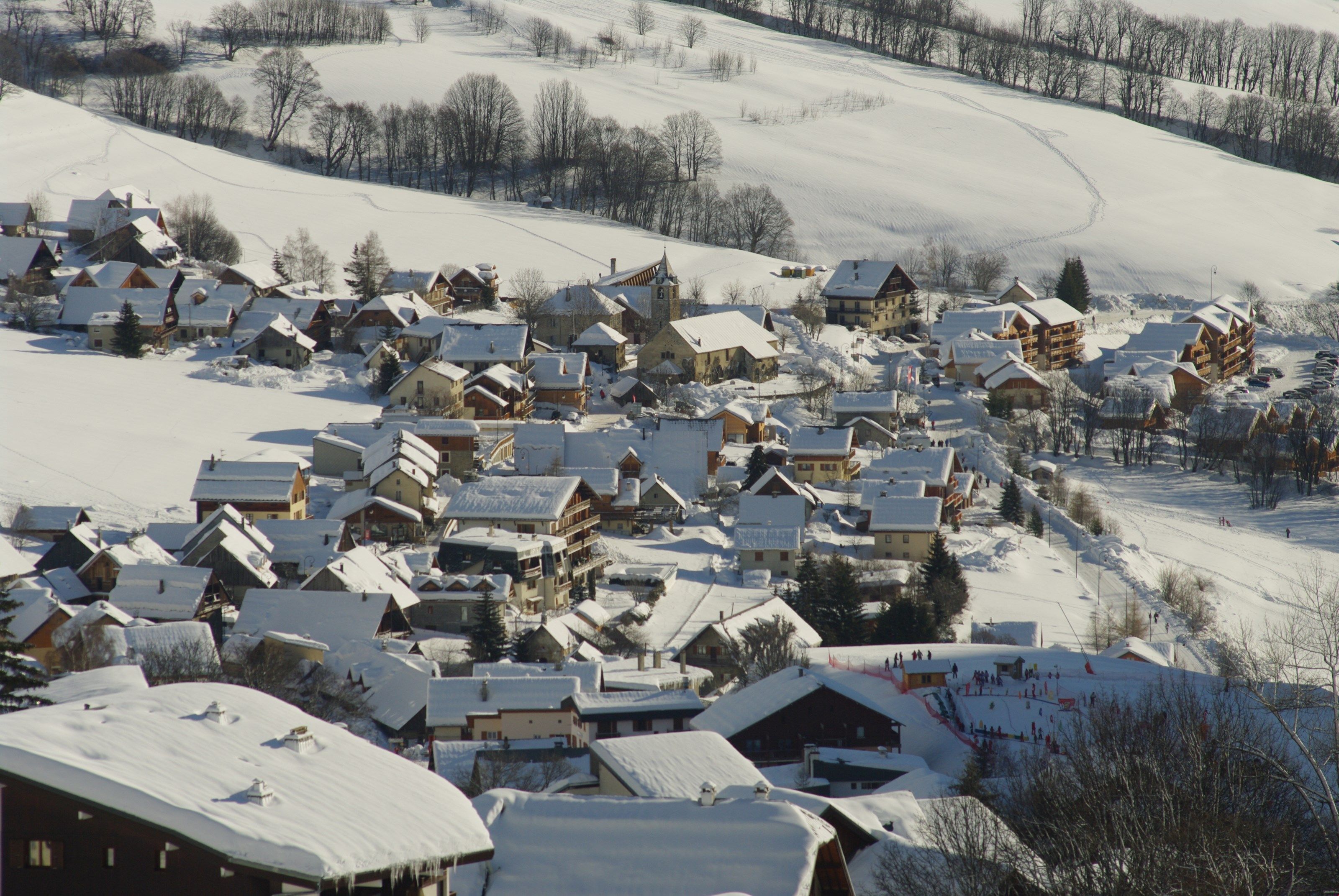 Un village enneigé, avec ses maisons traditionnelles en bois et une piste de ski.