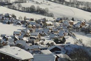 Un villaggio innevato con case in legno tradizionali, una pista da sci e un cielo sereno.