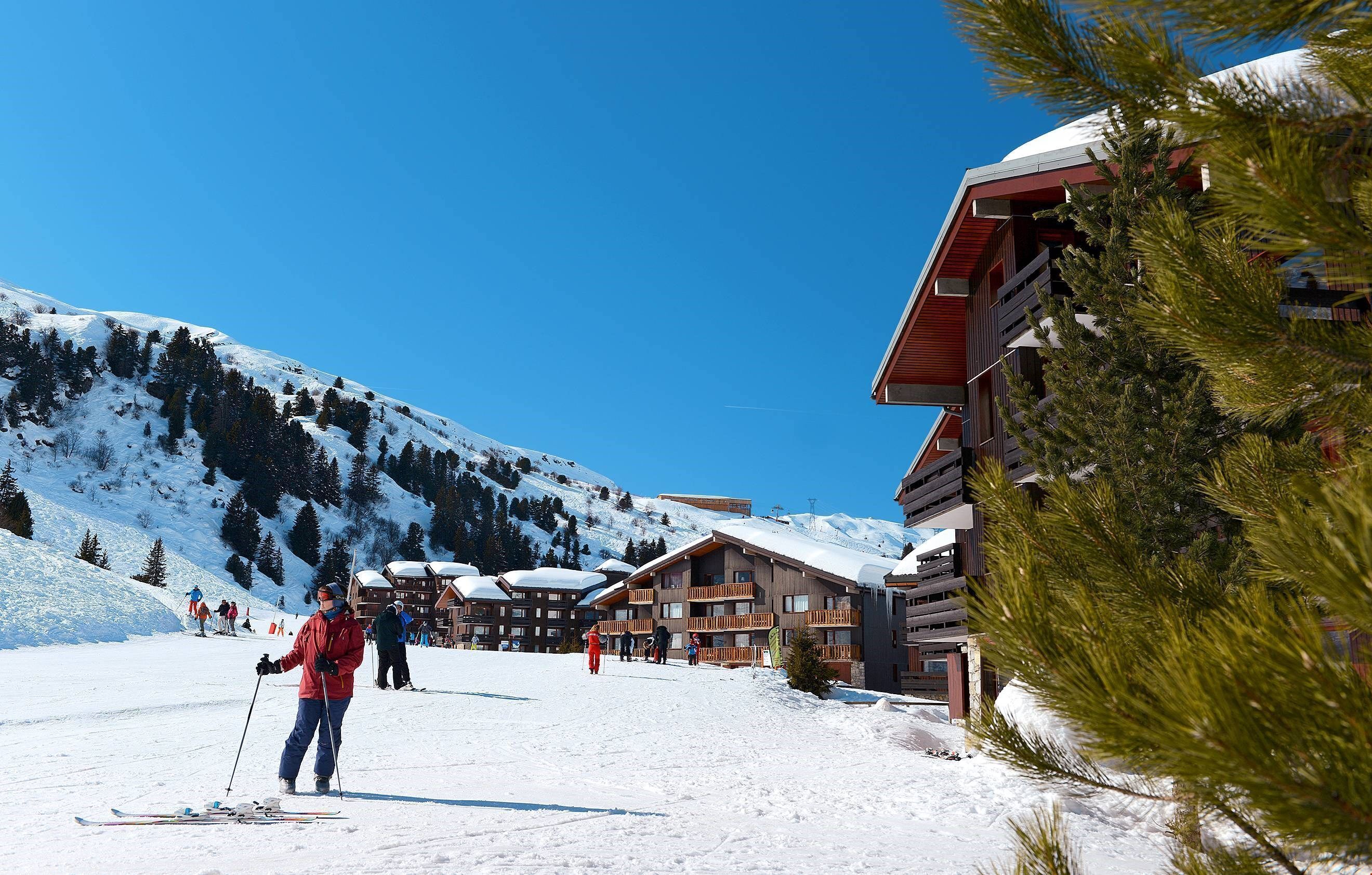 Een skigebied met houten gebouwen, besneeuwde pistes en skiërs.