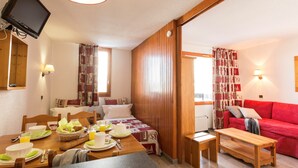 Een gezellige kamer met een ontbijttafel, een bed met quilt, een rode bank en een houten vloer.