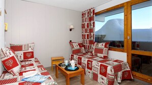 Ein gemütliches Zimmer mit einer rot-weißen gesteppten Sofagarnitur, einem kleinen Holztisch mit Tablett und einem Fenster mit Vorhängen.
