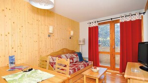 A cozy room with a wooden wall, a sofa with patterned cushions, a dining table with a map, and a television on a wooden table.