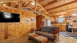 Ein Holzblockhaus-Innenraum mit Wohnbereich, Sofa, Couchtisch, Flachbildfernseher, Küchenzeile und einem karierten Boden.