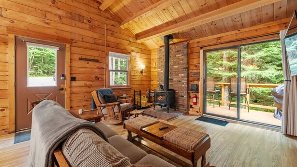 Ein gemütliches Blockhaus-Interieur mit Kamin, Holzmöbeln und Blick auf den Wald.