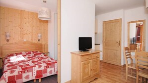 A bedroom with a wooden headboard, a bed with a red and white patterned bedspread, a wooden nightstand with a television, and a wooden wardrobe. - Sleeps 8 | 2BR Alcove in Prime Ski Location! (Valmeinier)