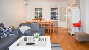 Un salon avec un canapé gris, une table basse blanche et un fauteuil rouge. On y trouve également un coin repas avec des meubles en bois et un réfrigérateur blanc.