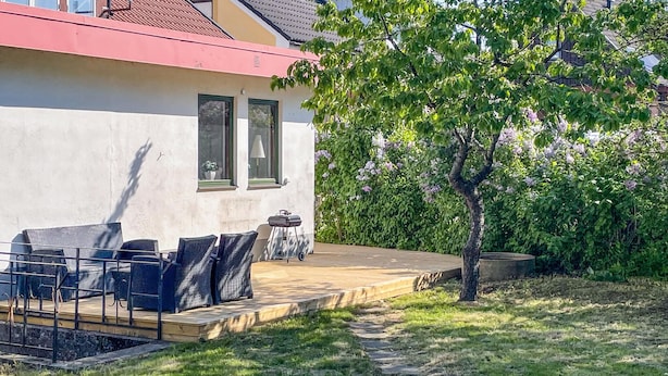 Une maison avec un patio, du mobilier d’extérieur et un arbre.