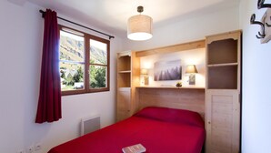 Ein Schlafzimmer mit Bett, einem Fenster mit Bergblick, einem Regal mit Lampe und einer Tür.
