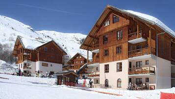 Un bâtiment de style chalet en bois, doté de nombreux balcons, avec une piste de ski au premier plan.