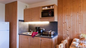 Una cocina compacta con armarios de madera, microondas, cafetera y lavamanos.