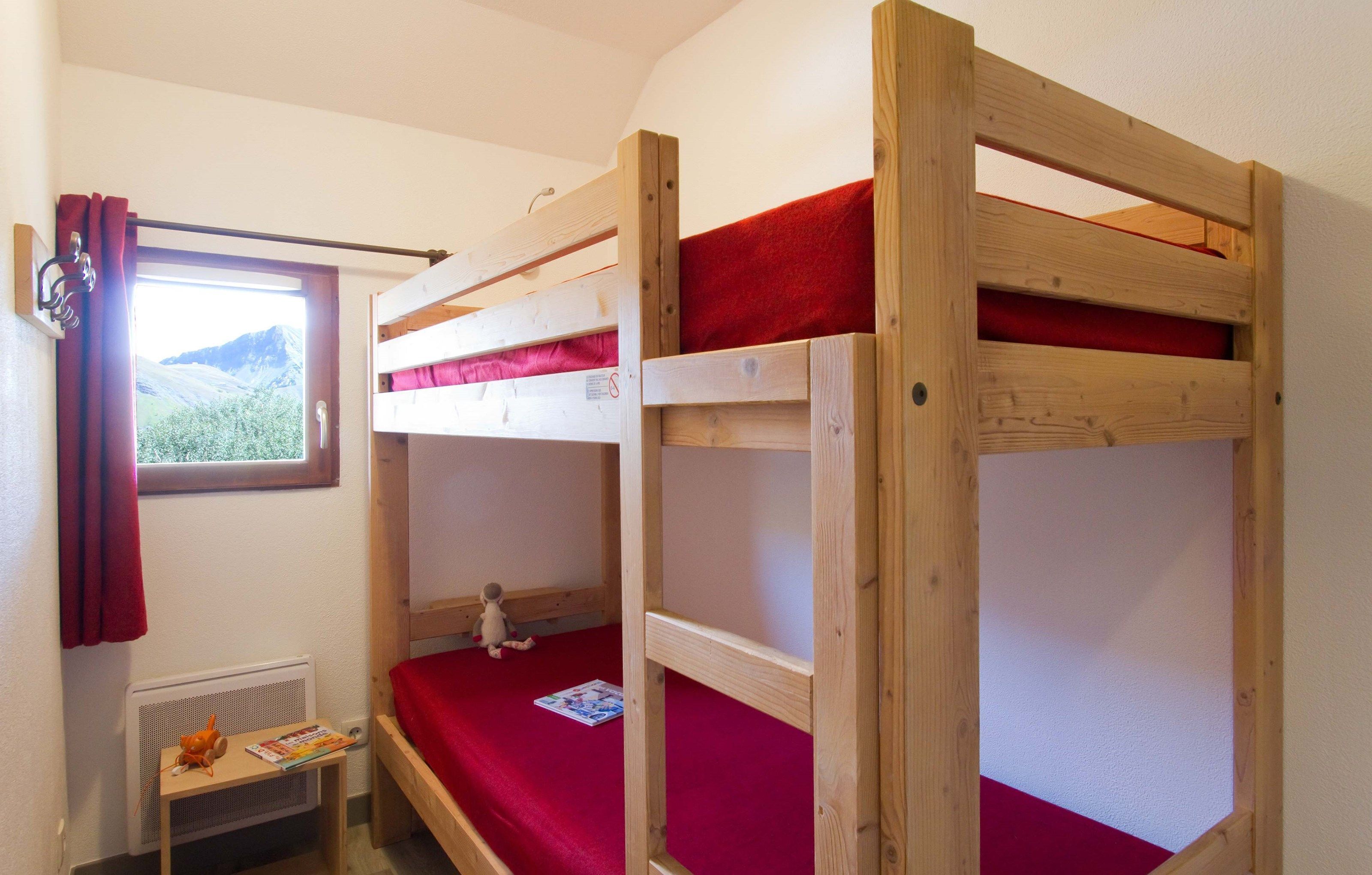A bunk bed room with a window, a radiator, and a small table with a book.