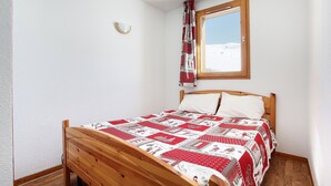 Un dormitorio con una cama de madera, una ventana que da a un paisaje nevado y una colcha con estampado rojo y blanco.